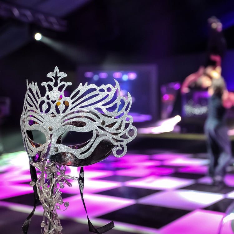 Venetian mask in front of black and white dancefloor with pink lights